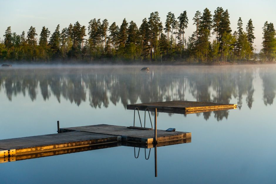 Tranquil misty lake scenery with reflections and wooden docks at dawn.